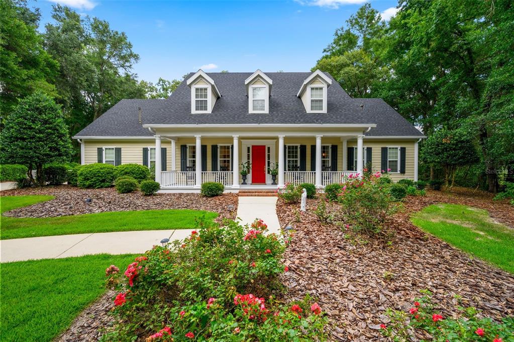 A yellow house with a covered front porch, a red door, and three roof dormers — 10005 SW 48TH PLACE, GAINESVILLE, FL