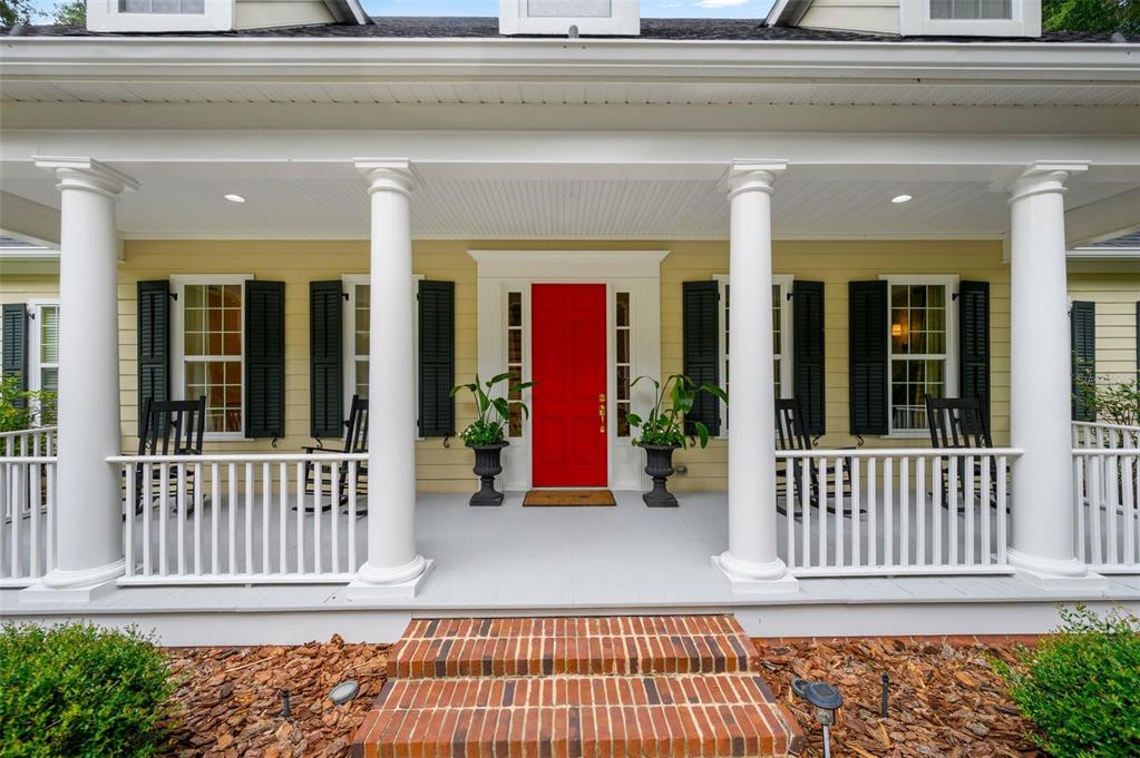A front porch features white columns, a bright red door, and black rocking chairs — 10005 SW 48TH PLACE, GAINESVILLE, FL