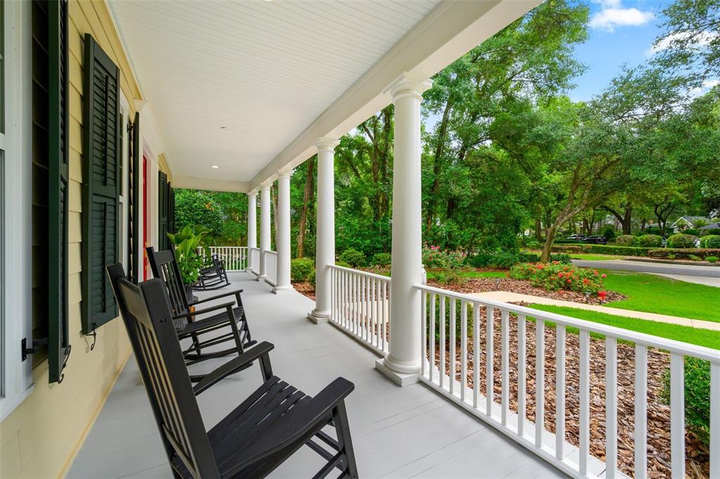 A covered front porch features black rocking chairs, white columns, and a view of landscaping — 10005 SW 48TH PLACE, GAINESVILLE, FL