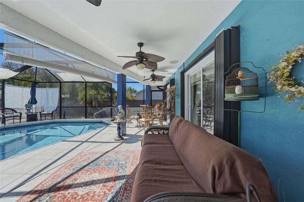 A covered patio features a brown sofa, a patterned rug, and a swimming pool enclosure — 19823 MIDWAY BOULEVARD, PORT CHARLOTTE, FL