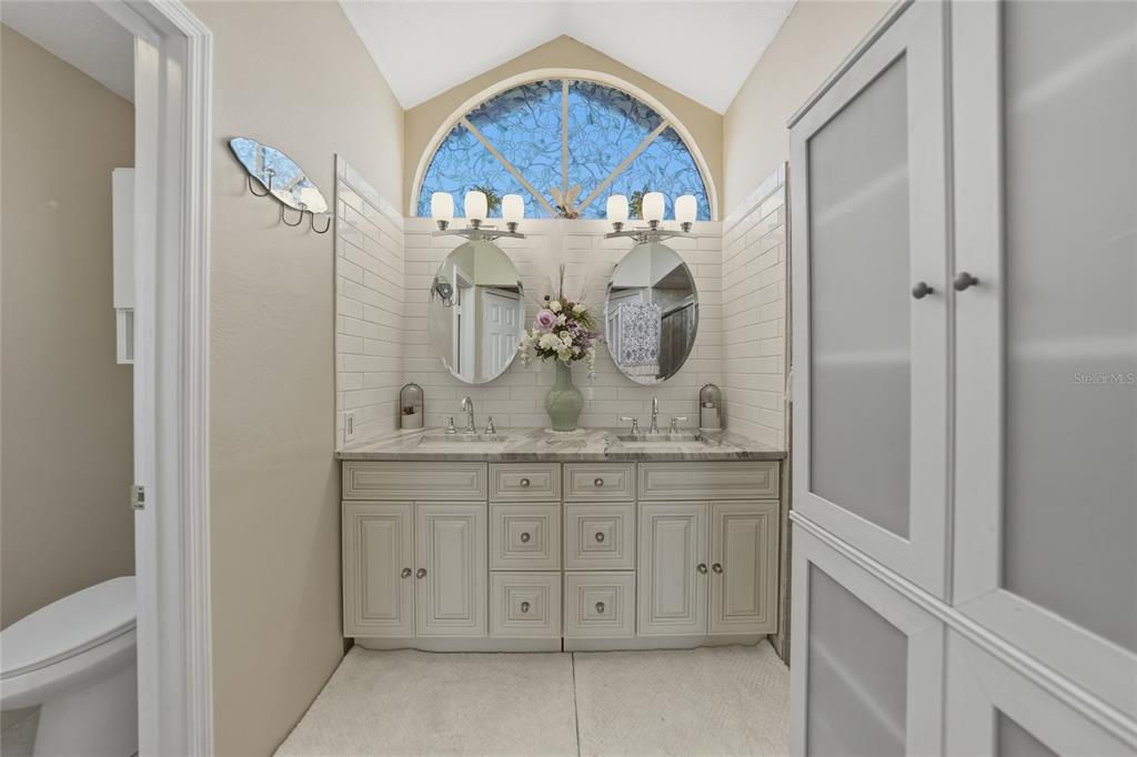 A bathroom features a double vanity with marble countertops, subway tile backsplash, and arched windows — 19823 MIDWAY BOULEVARD, PORT CHARLOTTE, FL