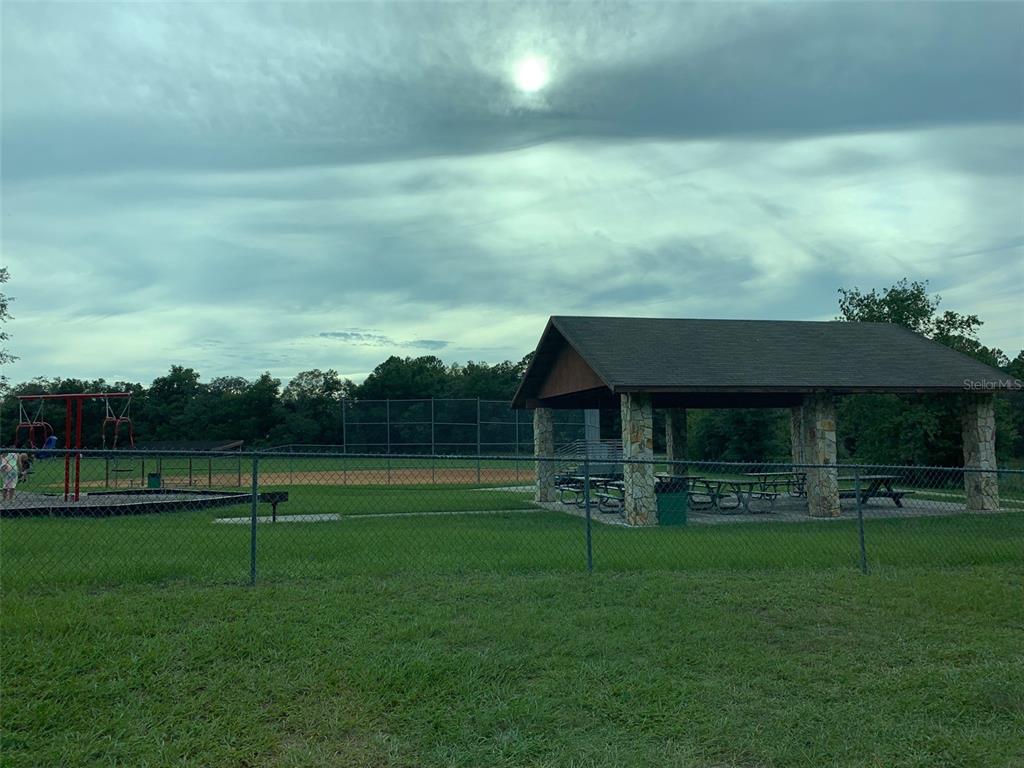 A park features a covered pavilion, a playground, and a fenced baseball field under a cloudy sky — 8178 N FEATHER AVENUE, DUNNELLON, FL