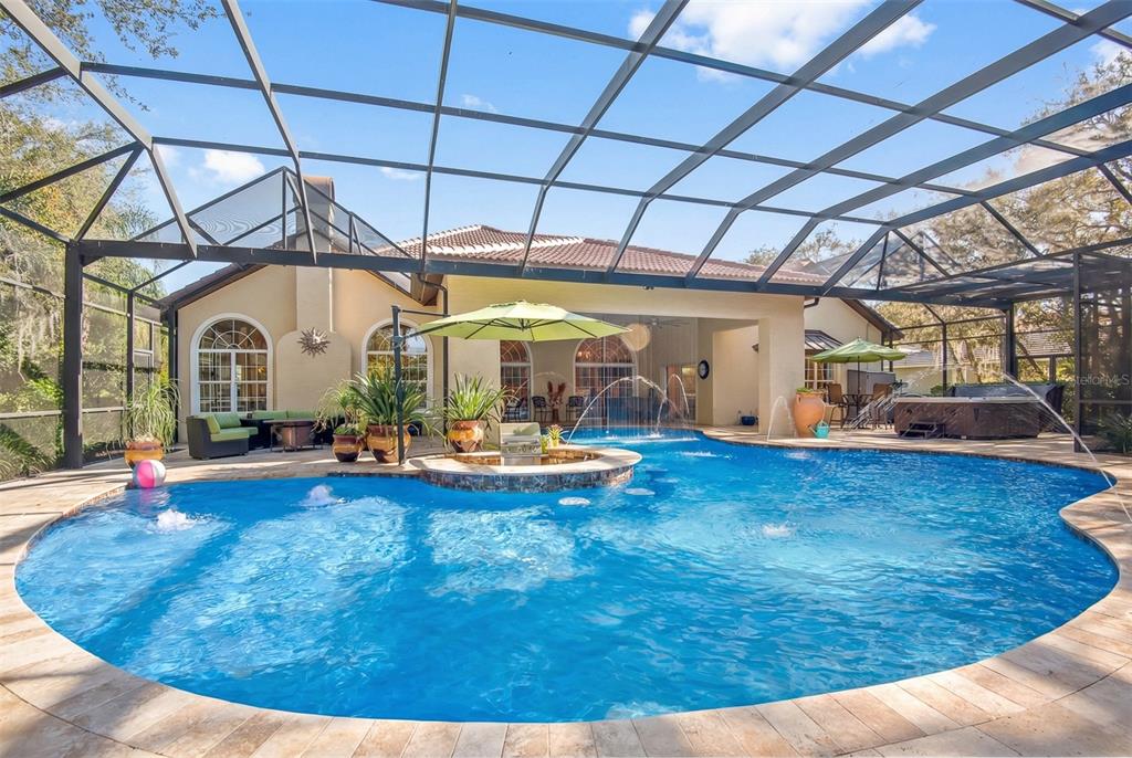 A screened-in swimming pool with a central fountain and spa sits behind a residential home — 8 RUE RENOIR, PALM COAST, FL