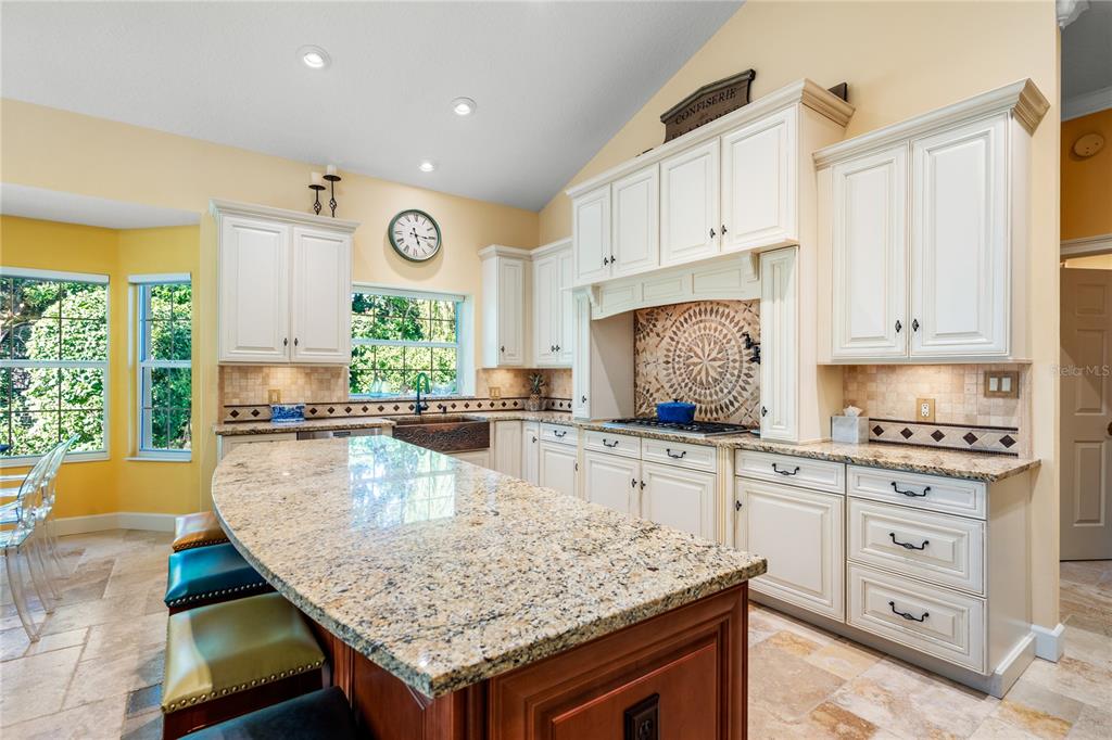 A kitchen features cream-colored cabinets, a granite-topped island, and a decorative tile backsplash — 8 RUE RENOIR, PALM COAST, FL