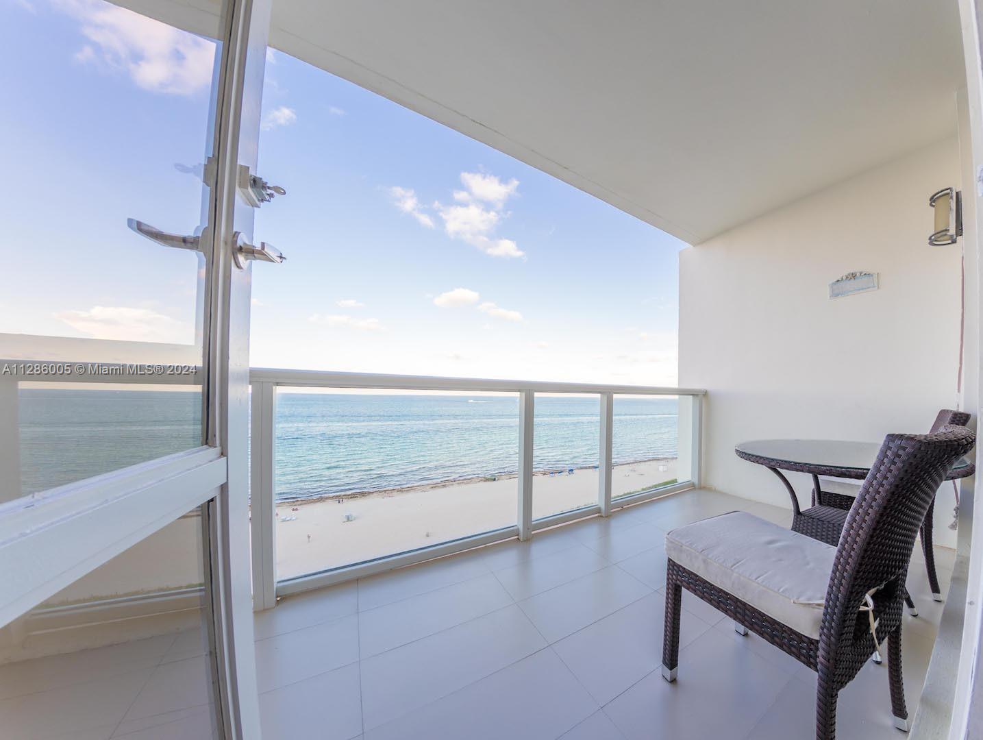 A balcony with a glass railing overlooks the beach and ocean with outdoor seating — 5601 Collins Ave # 1206, Miami Beach FL 33140, MIAMI BEACH, FL