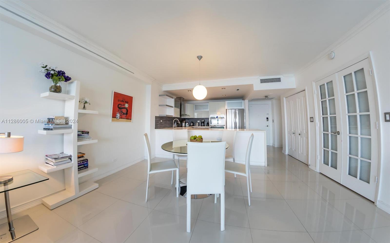 A bright dining area features a glass table, white chairs, and a modern kitchen — 5601 Collins Ave # 1206, Miami Beach FL 33140, MIAMI BEACH, FL