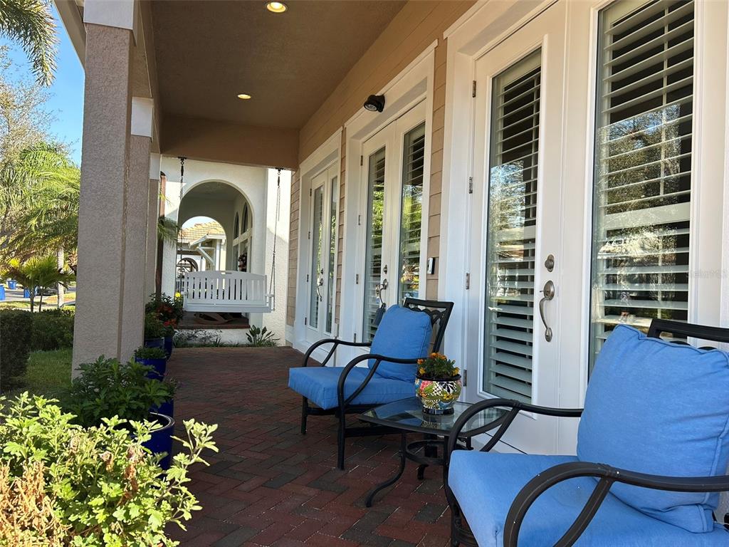 A covered brick porch features two blue chairs, a small table, and a hanging swing — 6101 YEATS MANOR DRIVE, TAMPA, FL