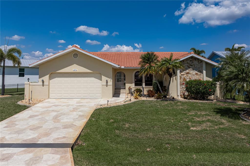 A single-story house with a tile roof, stone accent wall, and a paved driveway — 1374 WILLET COURT, PUNTA GORDA, FL