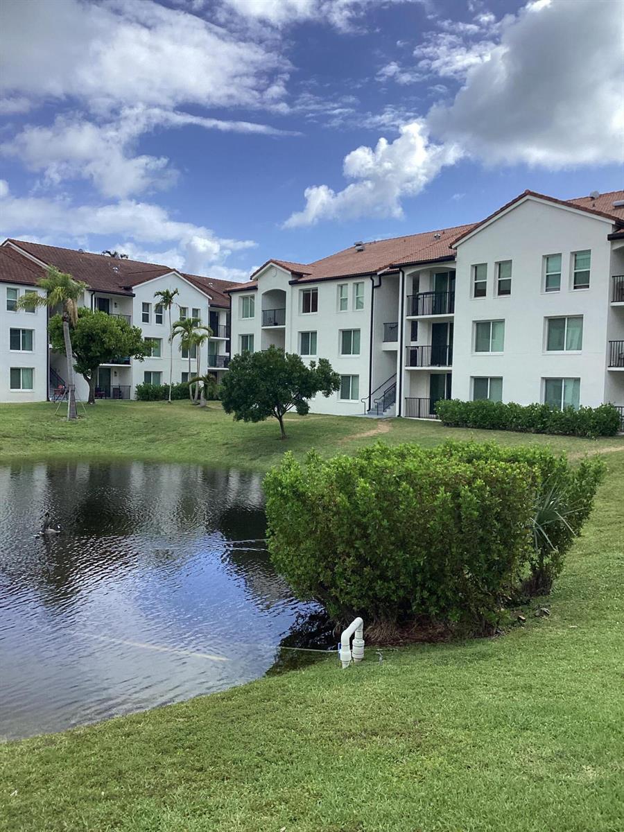 A multi-story apartment complex overlooks a small pond with a grassy foreground — 116 Villa Circle # 116, Boynton Beach FL 33435, BOYNTON BEACH, FL