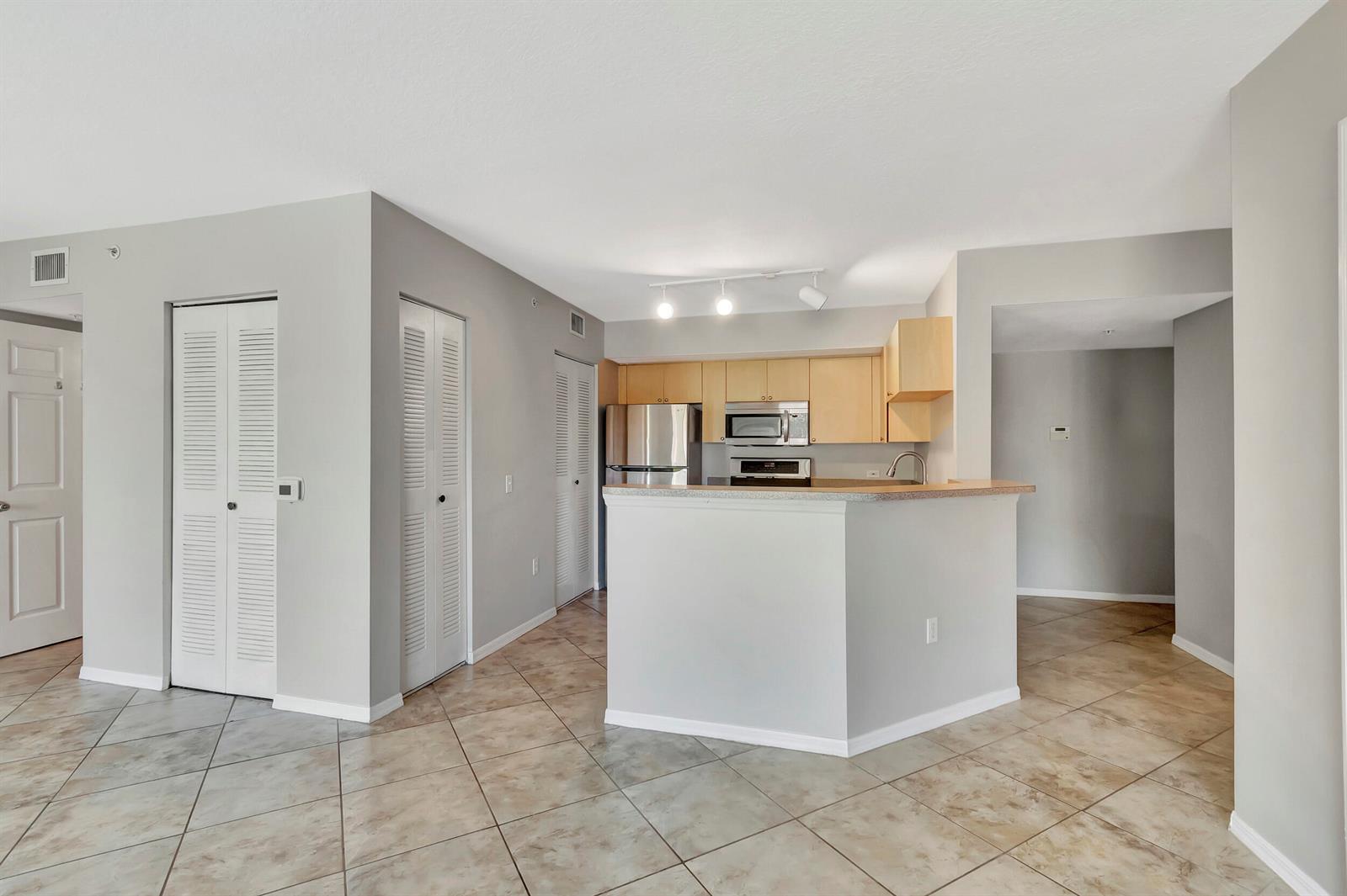 A kitchen with light wood cabinets and stainless steel appliances overlooks a tiled living area — 116 Villa Circle # 116, Boynton Beach FL 33435, BOYNTON BEACH, FL