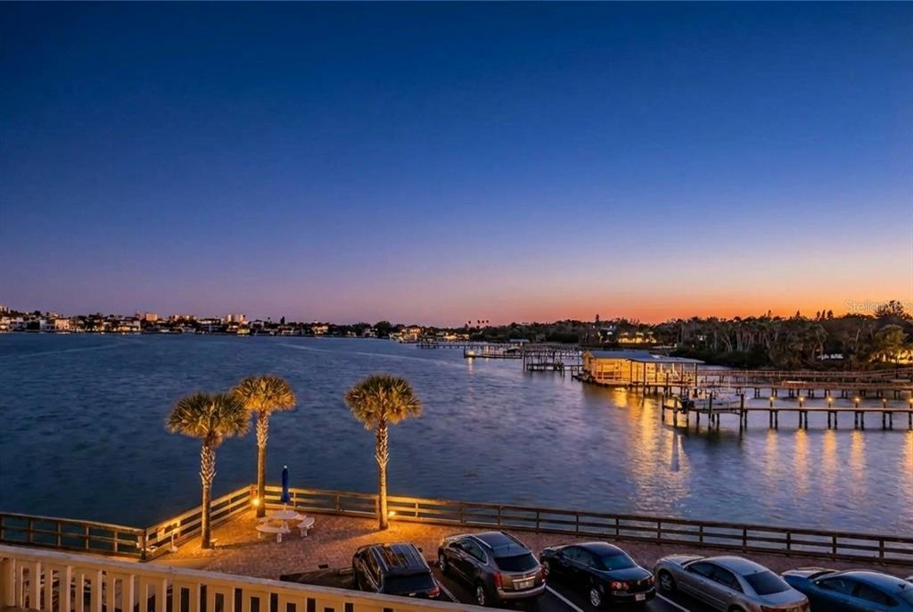 An elevated view of a waterfront parking area with palm trees and boat docks at sunset — 100 BLUFF VIEW DRIVE UNIT 514C, BELLEAIR BLUFFS, FL