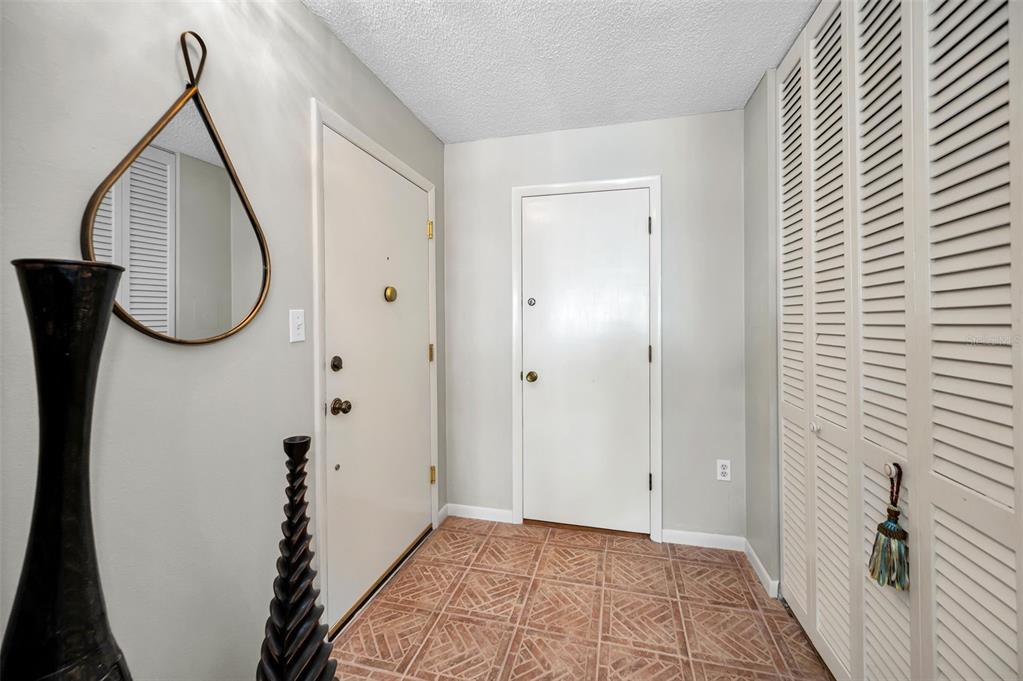 An entryway features tiled floors, two white doors, a teardrop-shaped mirror, and louvered closet doors — 100 BLUFF VIEW DRIVE UNIT 514C, BELLEAIR BLUFFS, FL