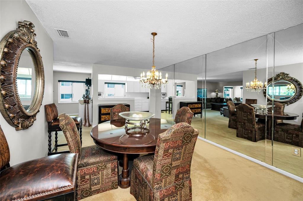 A dining area features a round wooden table, patterned chairs, a chandelier, and mirrored walls — 100 BLUFF VIEW DRIVE UNIT 514C, BELLEAIR BLUFFS, FL
