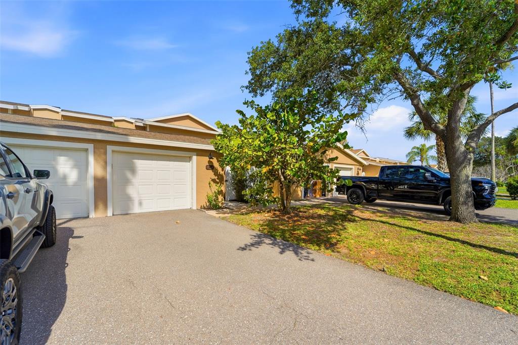 A tan townhouse exterior with two garage doors, a paved driveway, and a parked pickup truck — 833 E GULF BOULEVARD UNIT 103, INDIAN ROCKS BEACH, FL