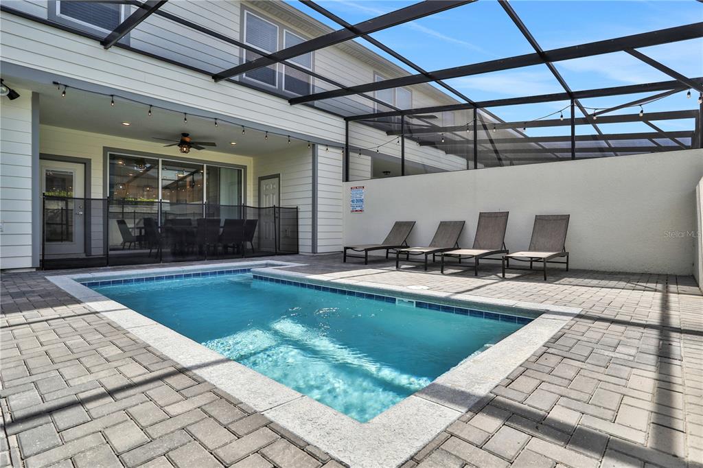 A screened-in patio features a rectangular swimming pool, four lounge chairs, and brick pavers — 900 PARADISE DRIVE, DAVENPORT, FL