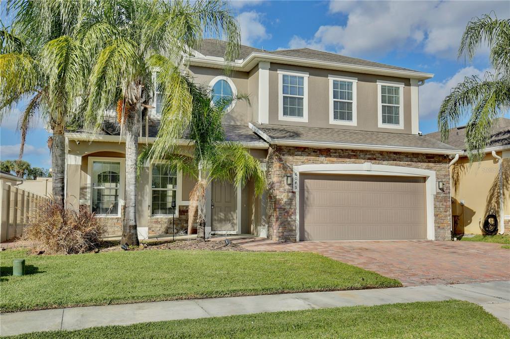 A two-story house with a stone facade, a two-car garage, and palm trees in front — 6049 FENDER COURT, ORLANDO, FL