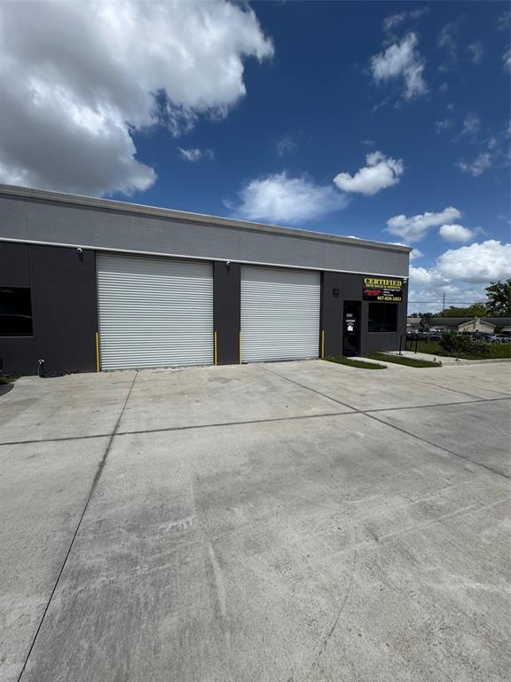 The exterior of a commercial building features two large roll-up garage doors and a sign — 4825 OLD WINTER GARDEN ROAD, ORLANDO, FL