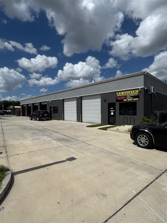 A commercial building with multiple garage bays and a parking lot under a cloudy sky — 4825 OLD WINTER GARDEN ROAD, ORLANDO, FL