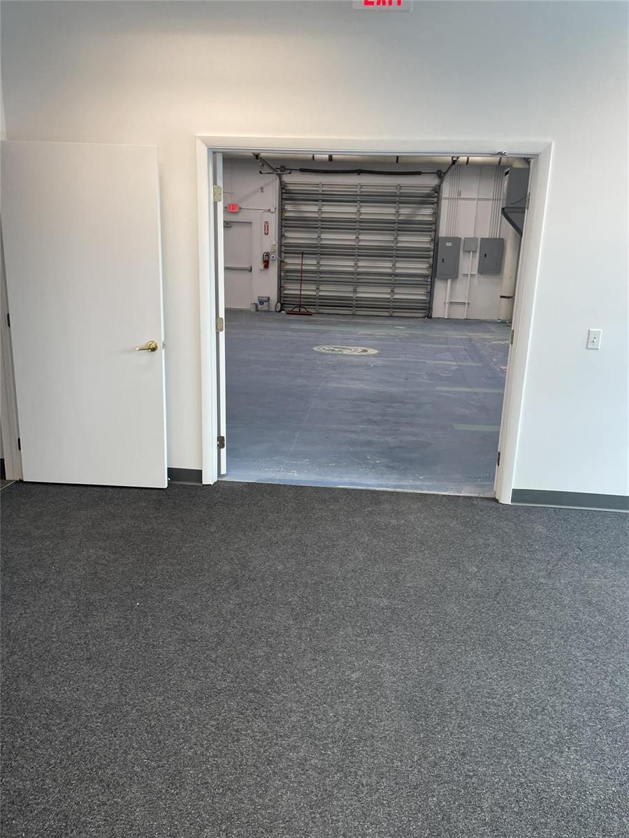 A carpeted office room opens into a warehouse space with a large metal roll-up door — FORT LAUDERDALE, FL