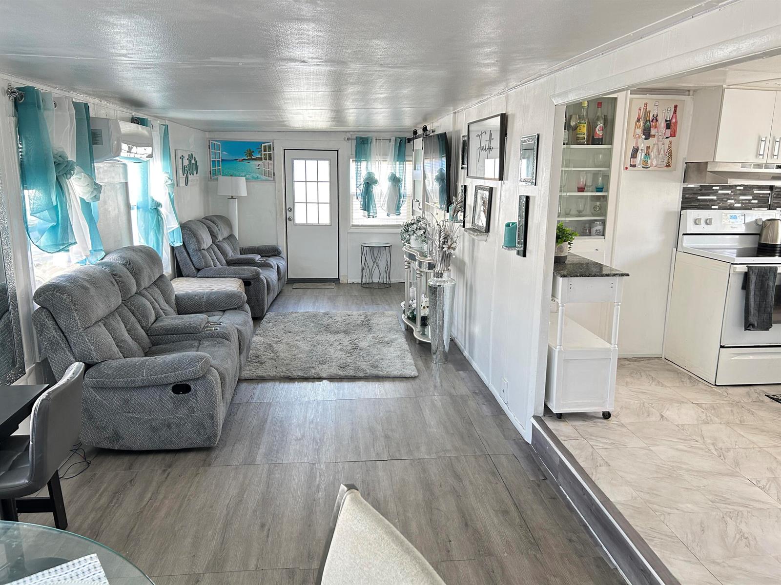 A living room with gray reclining furniture, wood-look flooring, and an adjacent white kitchen — 1325 S 33 Road, Hollywood FL 33021, HOLLYWOOD, FL