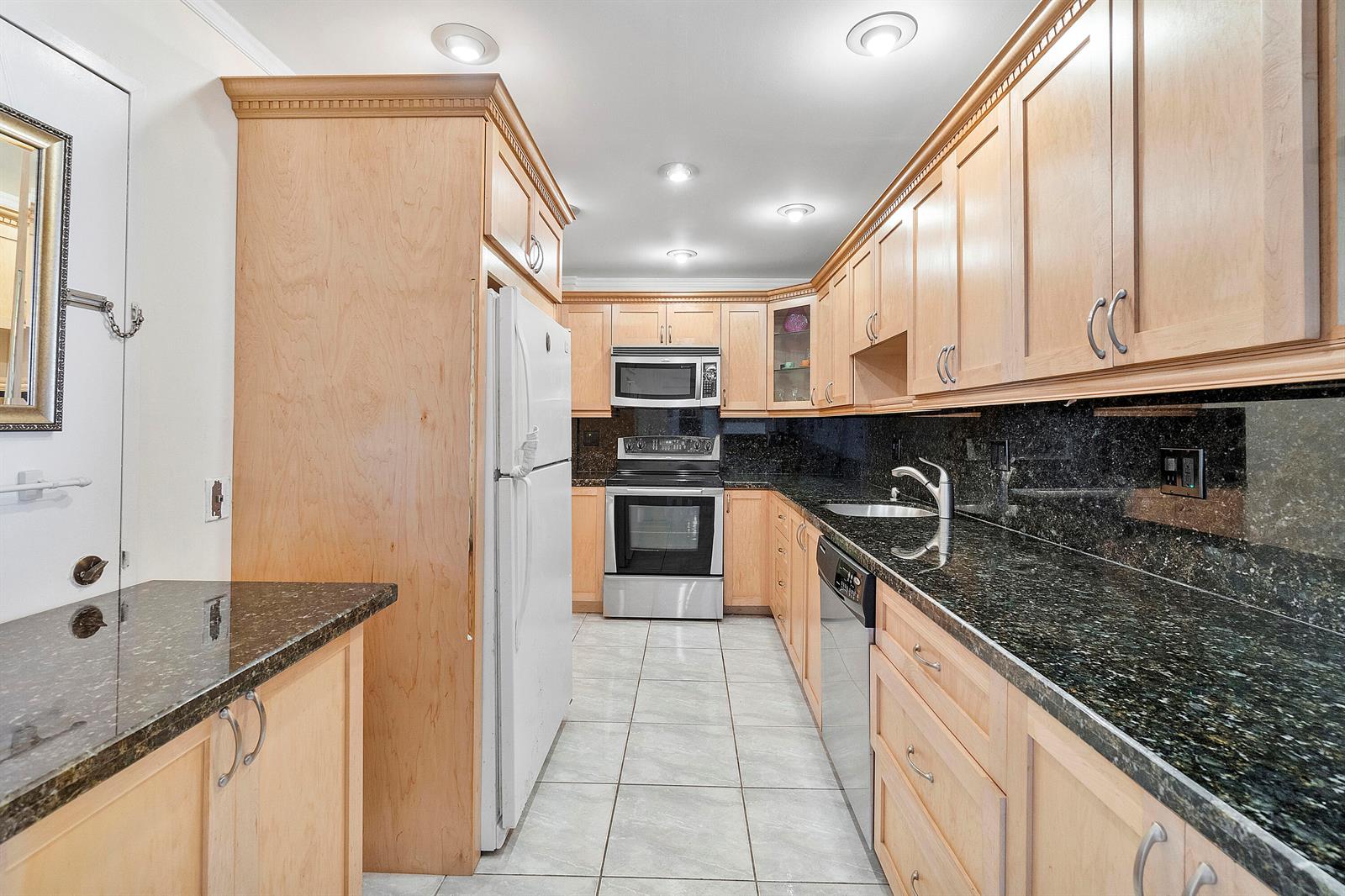 A galley kitchen features light wood cabinets, dark granite countertops, and stainless steel appliances — 2851 S Ocean Boulevard # B, Boca Raton FL 33432, BOCA RATON, FL