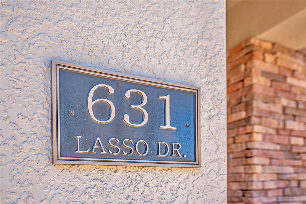 A metal address plaque is mounted on a textured stucco wall next to stone siding — 631 LASSO DRIVE, KISSIMMEE, FL