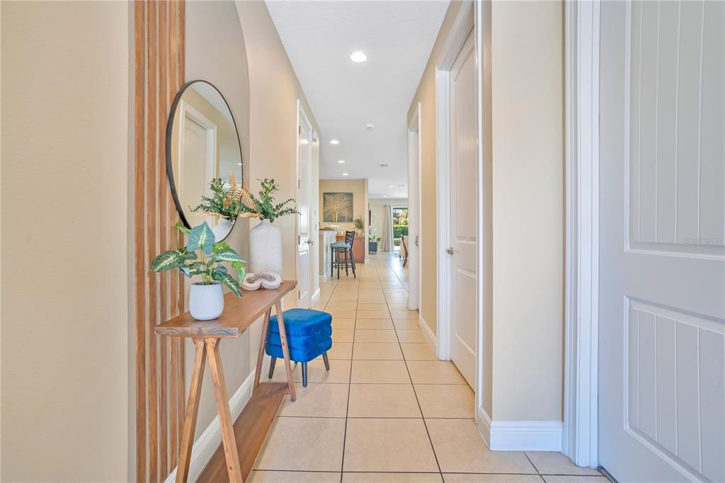 A tiled hallway features a wooden console table, a round mirror, and blue seating — 631 LASSO DRIVE, KISSIMMEE, FL