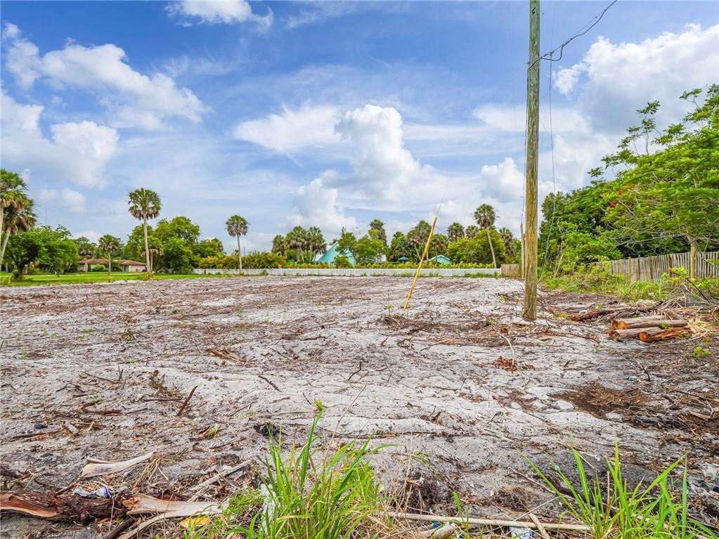 A cleared, sandy vacant lot features a utility pole and surrounding trees under a blue sky — 445 Old Dixie Highway, Vero Beach FL 32962, VERO BEACH, FL