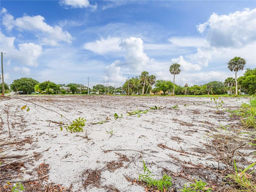 A flat, sandy, undeveloped lot features scattered debris and several palm trees under a cloudy sky — 445 Old Dixie Highway, Vero Beach FL 32962, VERO BEACH, FL