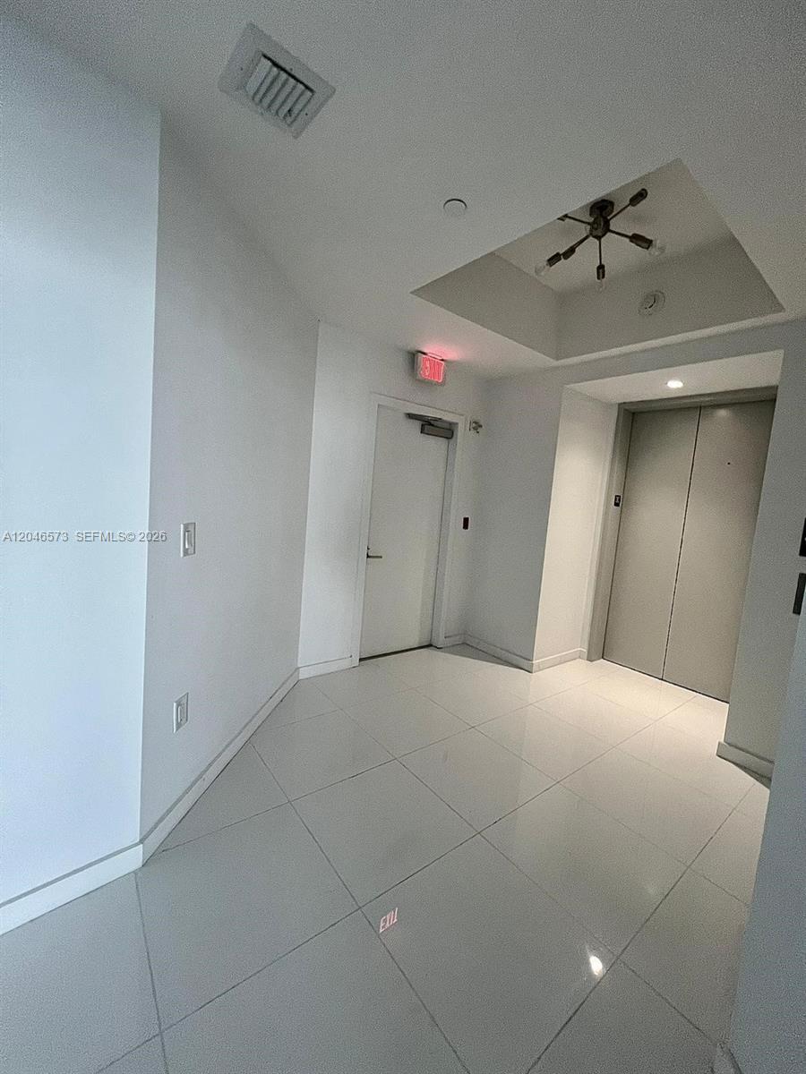 A modern hallway features white tile flooring, a recessed ceiling light fixture, and an elevator — MIAMI, FL