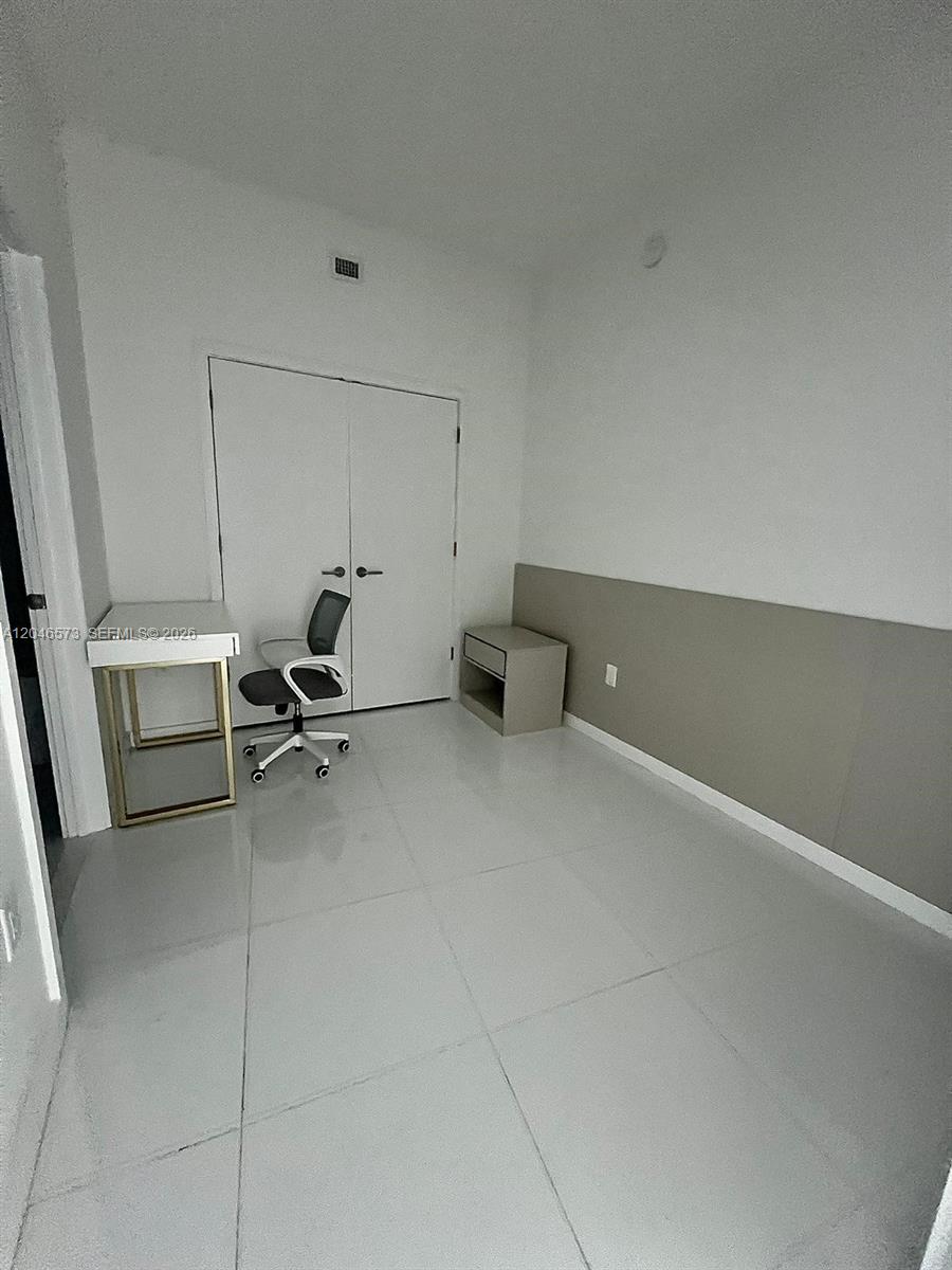 A small room features white tile flooring, a desk, a chair, and a closet — MIAMI, FL