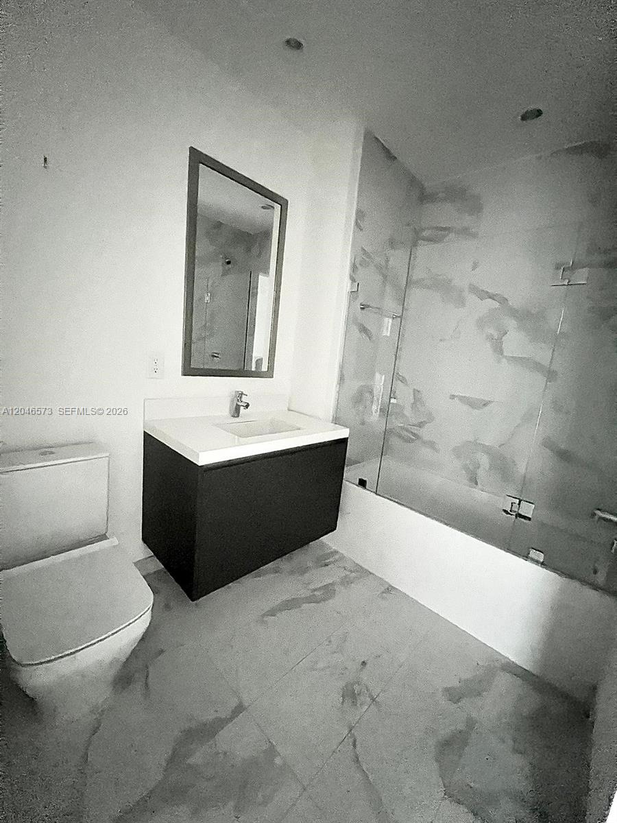 A modern bathroom features a floating vanity, a toilet, and a glass-enclosed bathtub shower — MIAMI, FL
