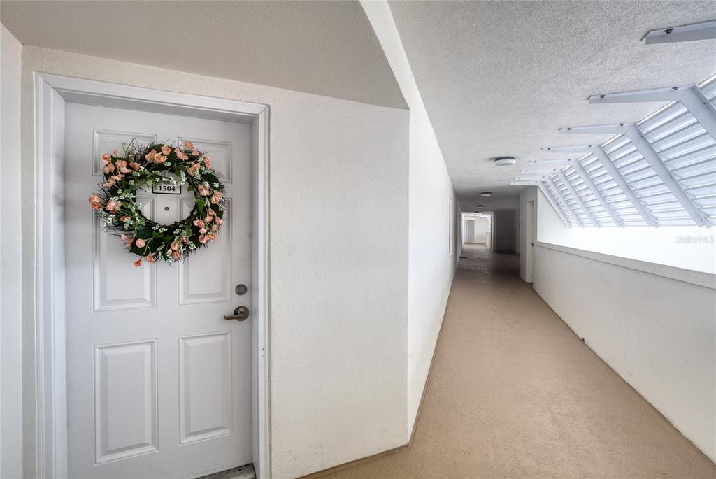 A white door with a floral wreath opens onto an outdoor apartment building hallway — 2937 S ATLANTIC AVENUE UNIT 1504, DAYTONA BEACH, FL