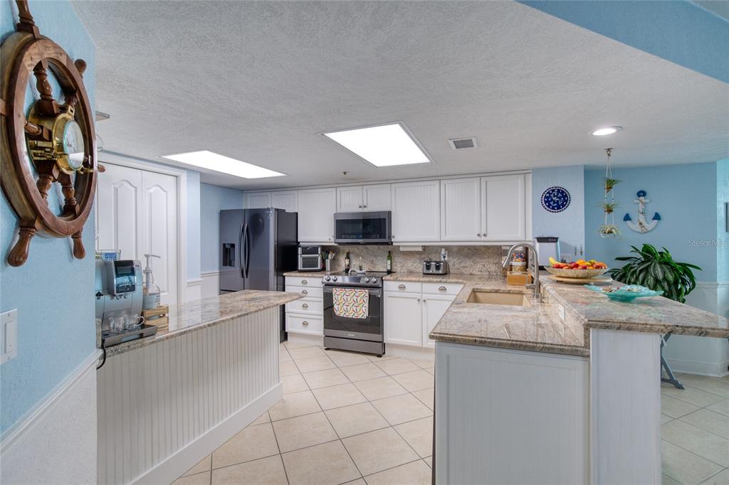 A kitchen features white cabinetry, granite countertops, stainless steel appliances, and light-colored tile flooring — 2937 S ATLANTIC AVENUE UNIT 1504, DAYTONA BEACH, FL