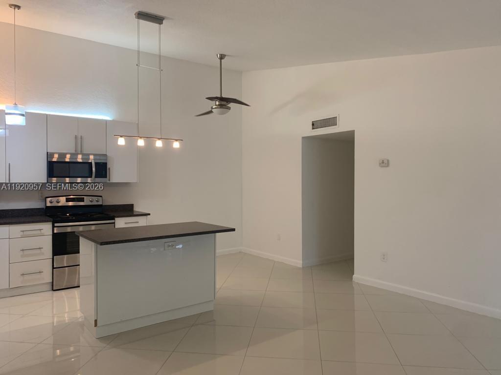 A modern kitchen features white cabinetry, a dark countertop island, and tile flooring — 907 NE 199th St # 204, Miami FL 33179, MIAMI, FL