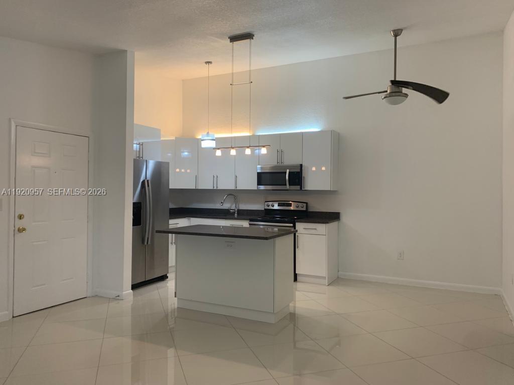 A modern kitchen features white cabinets, stainless steel appliances, a center island, and tile flooring — 907 NE 199th St # 204, Miami FL 33179, MIAMI, FL