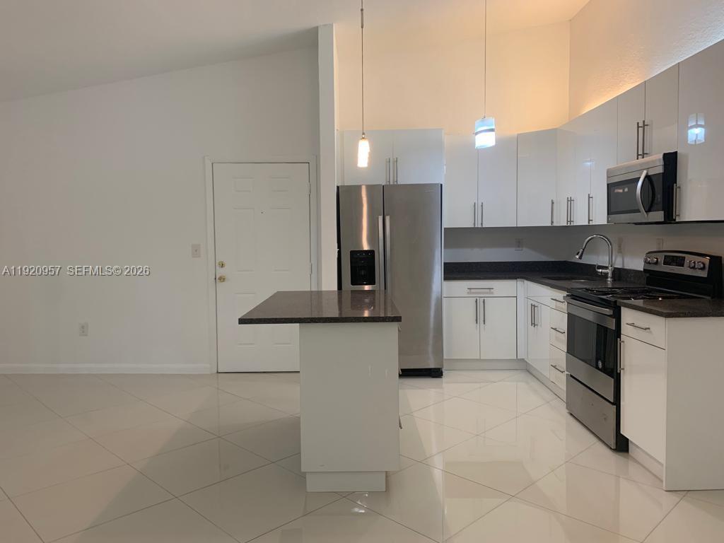 A modern kitchen features white cabinets, stainless steel appliances, and a dark granite island — 907 NE 199th St # 204, Miami FL 33179, MIAMI, FL