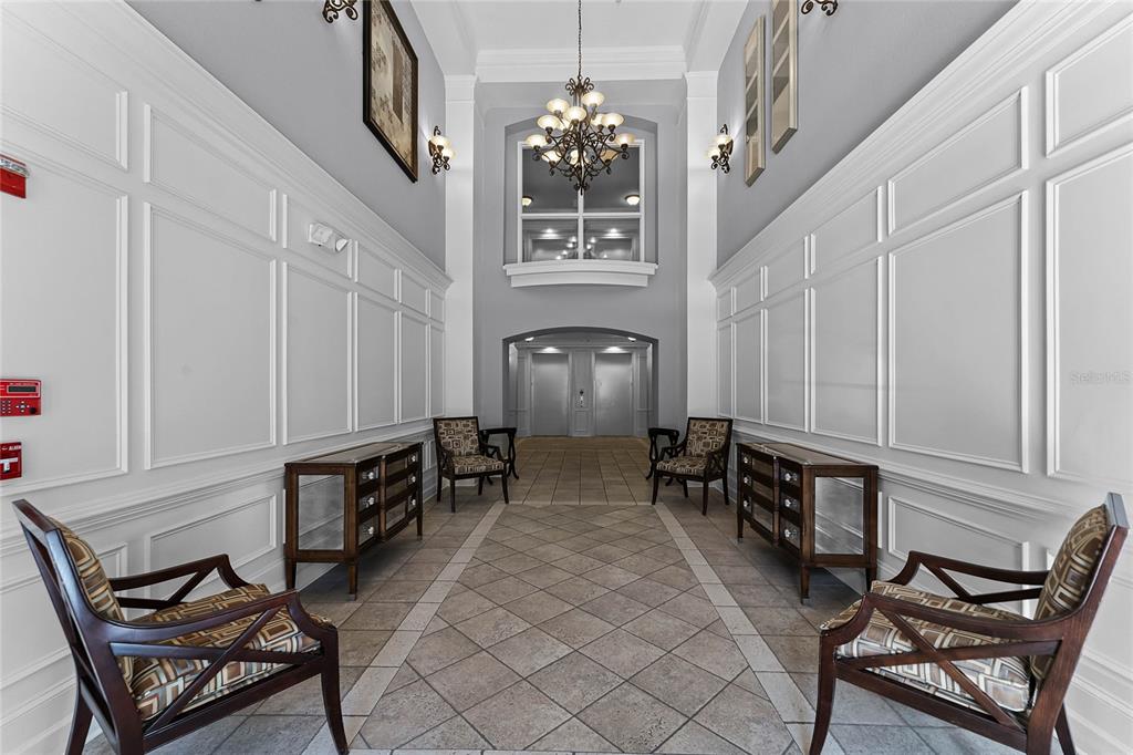 A symmetrical lobby features white paneled walls, tiled floors, four armchairs, and a central chandelier — 3356 ROBERT TRENT JONES DRIVE UNIT 101, ORLANDO, FL