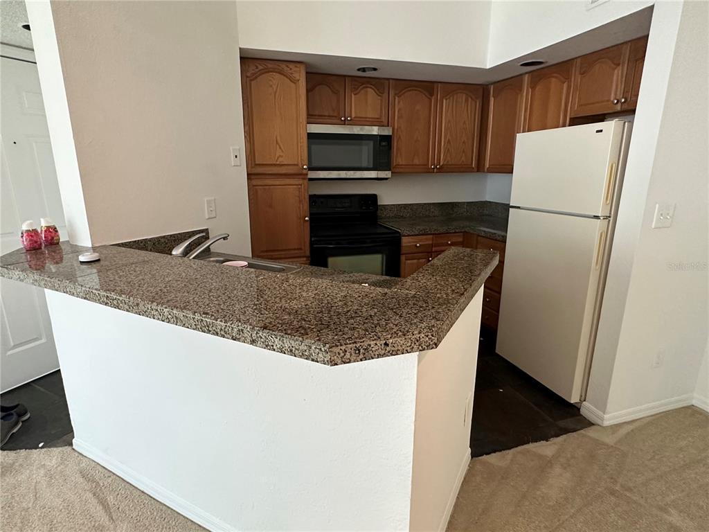 A kitchen features wood cabinets, granite countertops, a white refrigerator, and a breakfast bar — 4572 COMMANDER DRIVE UNIT 1234, ORLANDO, FL