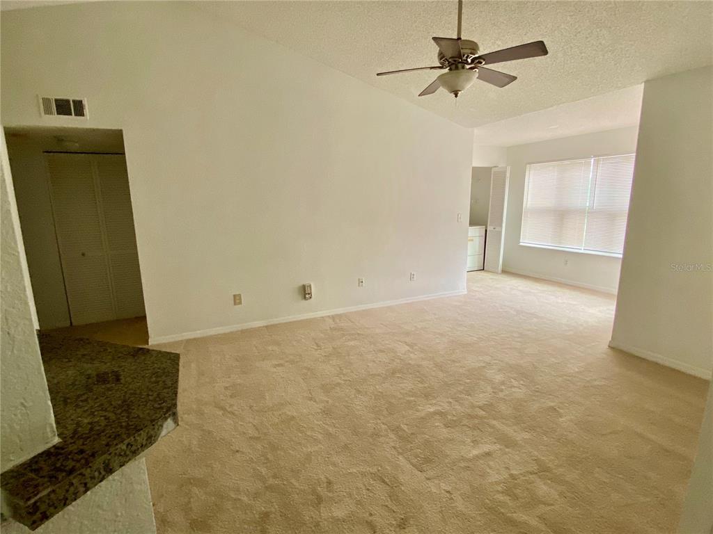 An empty living room features beige carpeting, a ceiling fan, and a large window — 4572 COMMANDER DRIVE UNIT 1234, ORLANDO, FL