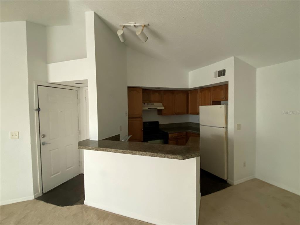 A kitchen with wood cabinets and a breakfast bar opens to a carpeted living area — 4572 COMMANDER DRIVE UNIT 1234, ORLANDO, FL