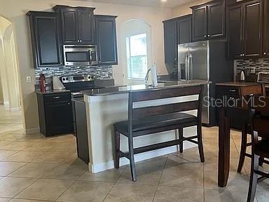 A kitchen features dark wood cabinets, stainless steel appliances, and a breakfast bar with seating — 4309 SUMMER BREEZE WAY, KISSIMMEE, FL