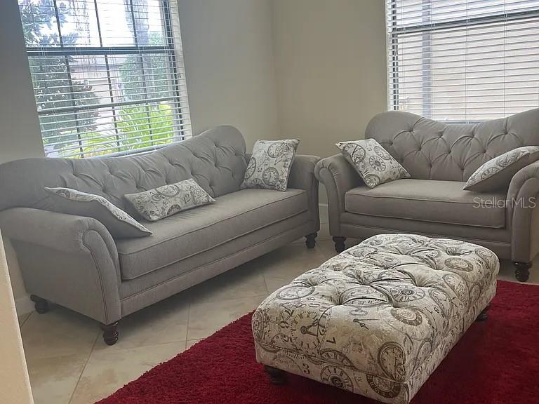 A living room features two gray tufted sofas, a patterned ottoman, and a red rug — 4309 SUMMER BREEZE WAY, KISSIMMEE, FL