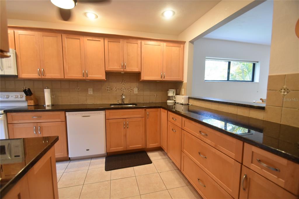 A kitchen features light wood cabinets, black countertops, and a white dishwasher on tiled floors — 1523 CLOWER CREEK DRIVE UNIT HA246, SARASOTA, FL