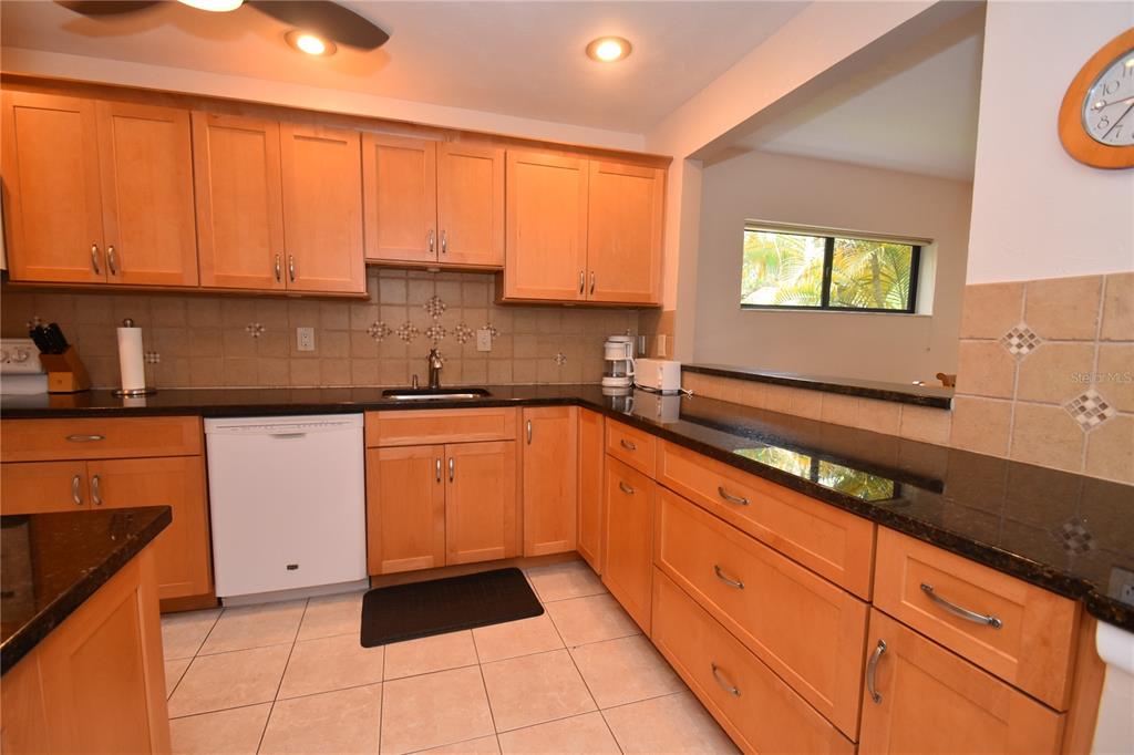 A kitchen features light wood cabinets, dark granite countertops, a white dishwasher, and tiled flooring — 1523 CLOWER CREEK DRIVE UNIT HA246, SARASOTA, FL