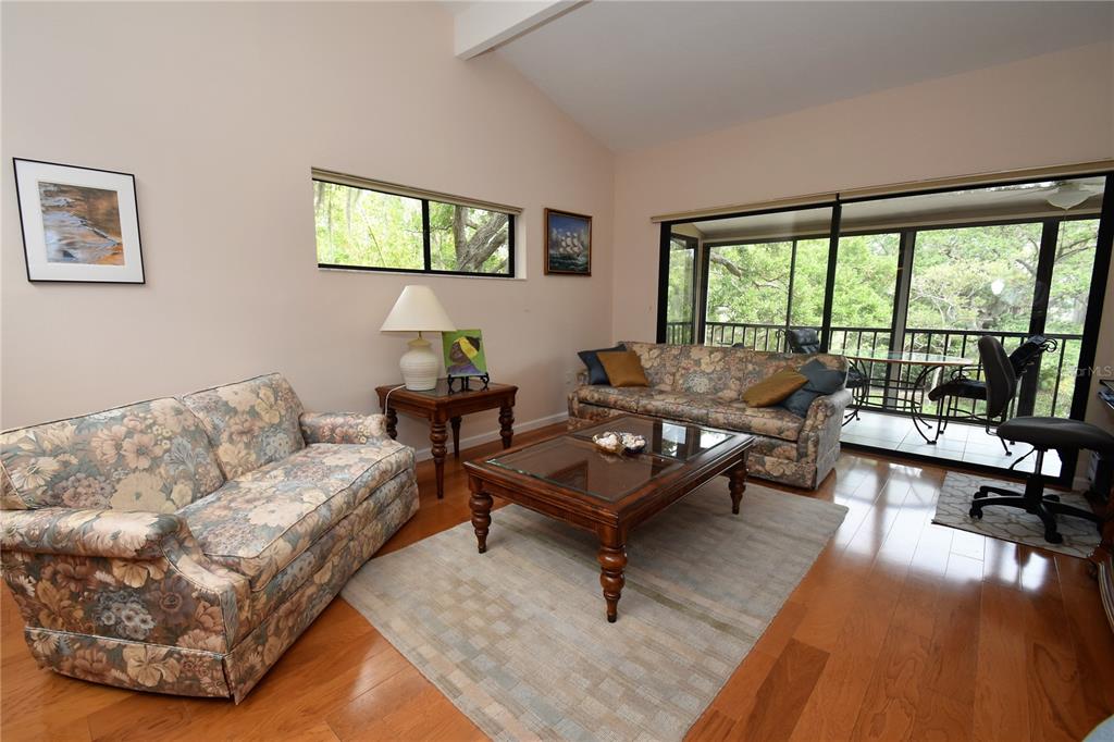 A living room features floral sofas, a wooden coffee table, hardwood floors, and a screened porch — 1523 CLOWER CREEK DRIVE UNIT HA246, SARASOTA, FL