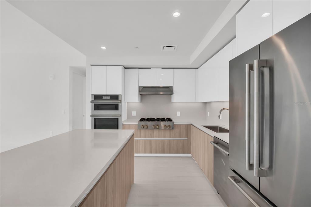 A modern kitchen features white upper cabinets, wood-tone lower cabinets, stainless steel appliances, and an island — 400 CENTRAL AVENUE UNIT 3606, ST PETERSBURG, FL