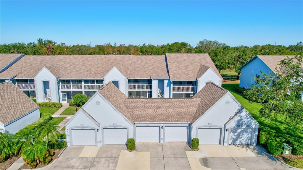 An aerial view of a multi-unit residential building featuring several garage doors and shingled roofs — 6713 STONE RIVER ROAD UNIT 205, BRADENTON, FL