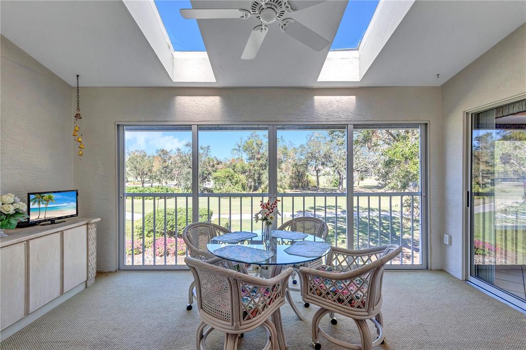 A sunroom with a glass dining table, skylights, and large windows overlooking a golf course — 6713 STONE RIVER ROAD UNIT 205, BRADENTON, FL