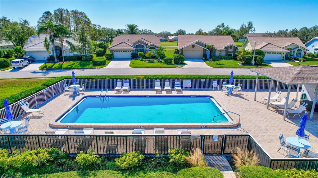 An outdoor swimming pool with lounge chairs and tables is surrounded by a black metal fence — 6713 STONE RIVER ROAD UNIT 205, BRADENTON, FL